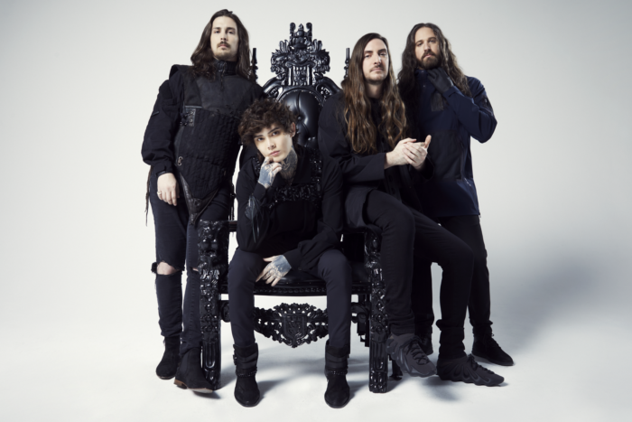The band Polyphia dressed in all black, with Tim Henson and Scott LePage sat upon a black throne